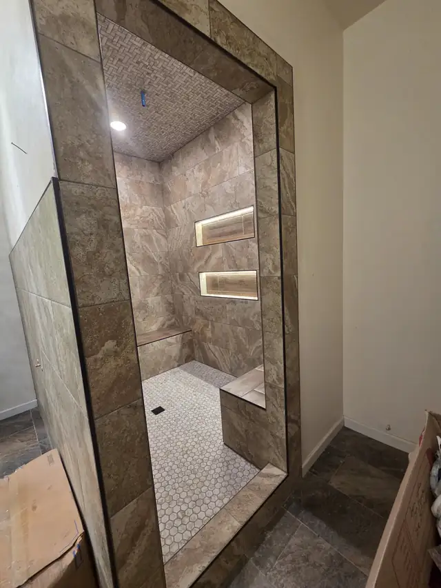 Tiled walk-in shower with travertine-look walls, a tile bench and two LED-lit niches